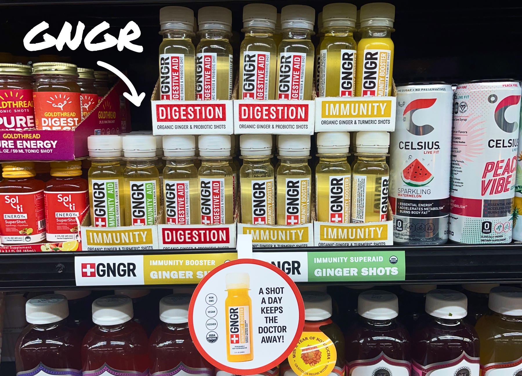 Shelves display GNGR ginger shots for Digestion and Immunity, benefit signs, a “A shot a day keeps the doctor away!” sign, and energy drinks.
