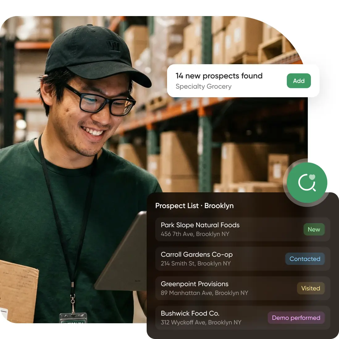 In a warehouse, a smiling person with glasses and a cap holds a tablet and box, tracking Brooklyn grocery store statuses onscreen.