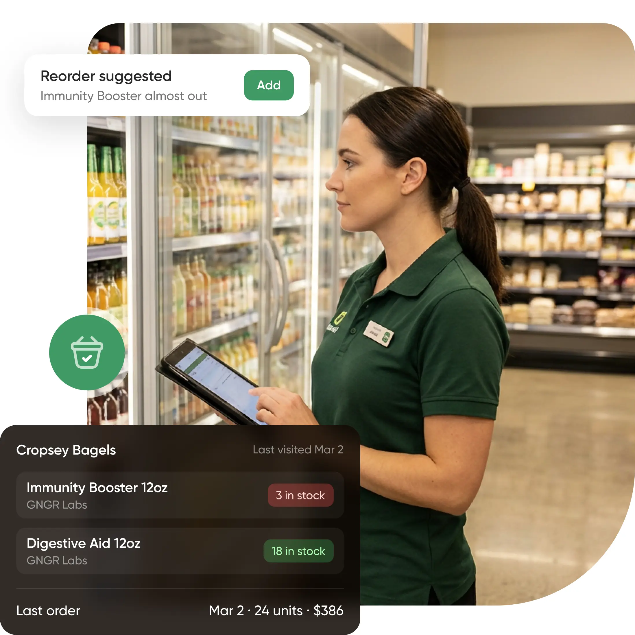 A woman in a green uniform checks grocery store shelves with a tablet, reviewing inventory data and seeing a low stock alert for Immunity Booster 12oz.