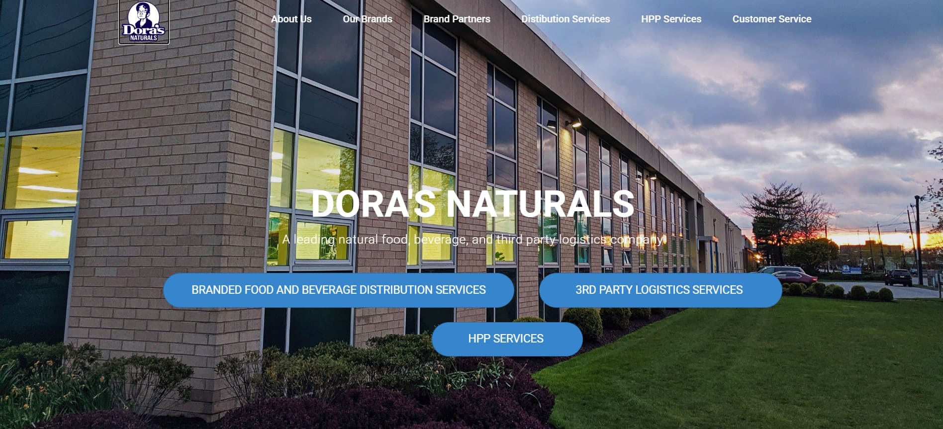Sunset shines on a modern brick office with large windows; Doras Naturals and navigation for delivery, logistics, and 2026 plans appear.