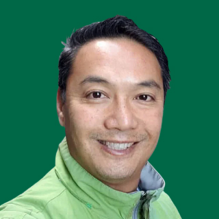 Happy man with short, dark hair in a light green jacket stands smiling against a solid green background, radiating positive energy.